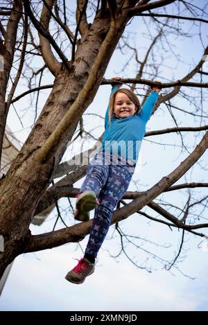 Young girl hanging from tree branch from above Stock Photo