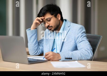 Focused Young Man Working At Desk With Laptop and Papers Stock Photo