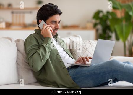 Young Man Talking on Phone While Working on Laptop Stock Photo