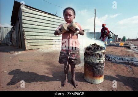 Picture by Roger Bamber : Barefoot Township kid in Soweto, South Africa uses shoes to keep his hands warm Stock Photo