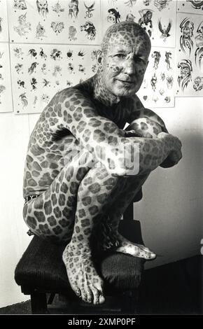 Tom Leppard, known as the Leopard Man of Skye. He spent Â£5,500 covering his body in leopard-like spots which he had done over more than a decade of visits to a Brighton Tattoo parlour. Here he has just had some more spots added in the 1990s.tattoo tattoos tattooed man leopard spots inked'tattoo parlour' [one 1 man] squatting sitting spotty spotted 'leopard man' extreme tattooing 'whole body' 'most tattooed man' 'Guinness Book of Records' 'world's most tattooed man' person 'body art' 'illustrated man' b/w b&w 'black and white' 90s 1990s 'Leopard man' Stock Photo