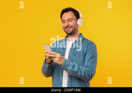 Happy Man Using Smartphone While Wearing Headphones Against Yellow Background Stock Photo