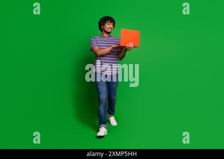 Photo portrait of young senior level programmer indian guy works online using laptop and walking isolated on green color background Stock Photo