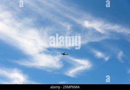 Abstract shapes formed by Cirrus clouds against a blue sky with silhouette of a passenger jet in sky Stock Photo