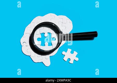 Magnifying glass placed on a human brain shaped puzzle with the final element to be set in place. Brain function and problem-solving concept. Stock Photo