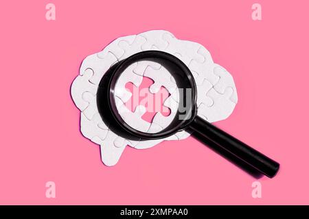 Flat human brain made of puzzle pieces placed under a magnifying glass on pink background. Psychology, brain study and exploration concept. Stock Photo
