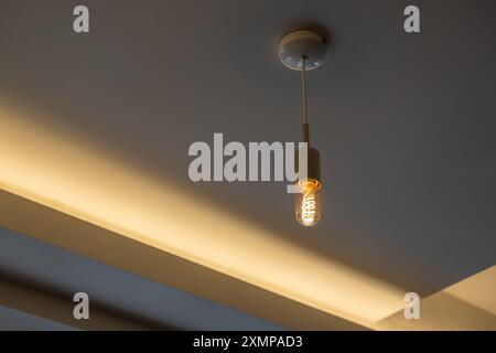 Hanging Edison light bulb, also known as filament light bulb. with ceiling cove lighting detail Stock Photo