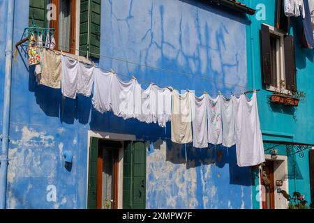 Drying clothes and towels hanging outside on rope against blue painted weathered facade of a house on Burano island in Venetian Lagoon, Italy. Stock Photo
