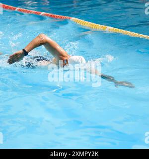 Dynamic image of young man, swimmer in motion, swimming freestyle stroke in pool outdoor on sunny day. Stock Photo