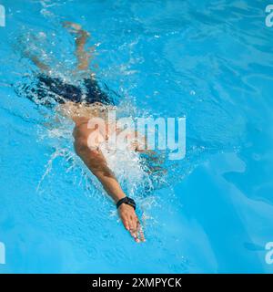 Dynamic image of young man, swimmer in motion, swimming freestyle stroke in pool outdoor on sunny day. Stock Photo