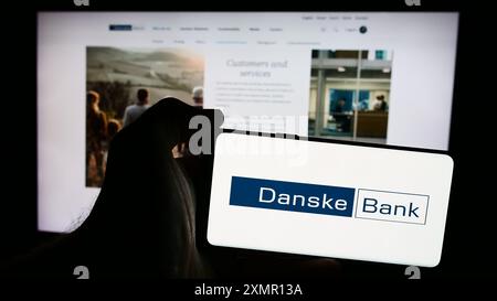 Person holding smartphone with logo of Danish financial services company Danske Bank AS in front of website. Focus on phone display. Stock Photo