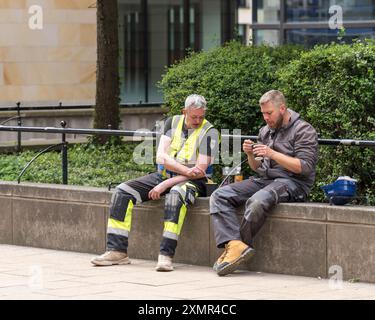 24 July 2024. Edinburgh,Scotland. This is 2 men sitting on a building wall opposite a building site eating their lunch of soup. Stock Photo