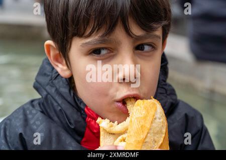 Boy biting traditional squid sandwich outdoors on Major Square at Madrid downtown in San Isidro Stock Photo