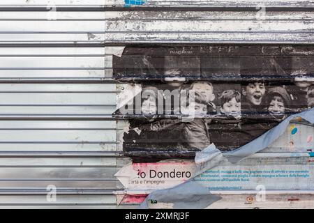 Milan, Italy - March 16, 2024: Torn old poster featuring black-and-white images of children, stuck to a shutter Stock Photo