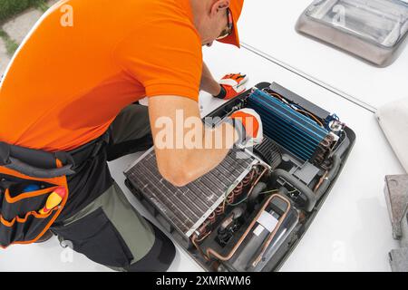 RV technician focused on servicing a rooftop air conditioning unit. He is carefully inspecting and adjusting components for optimal functionality unde Stock Photo