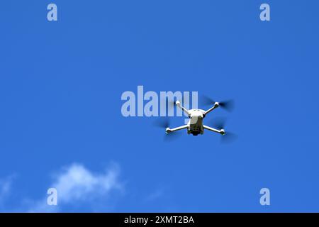 Small unmarked drone in flight isolated against a blue sky. No people. Stock Photo