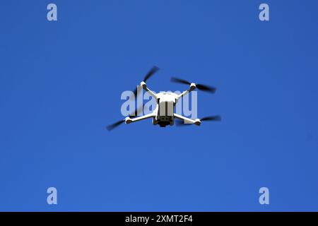 Small unmarked drone in flight isolated against a blue sky. No people. Stock Photo