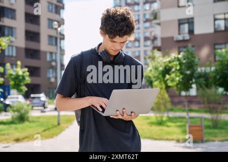 Young male college student with backpack headphones using laptop, outdoor Stock Photo