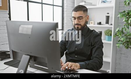 Handsome bearded man working intently on a computer in a modern office setting. Stock Photo