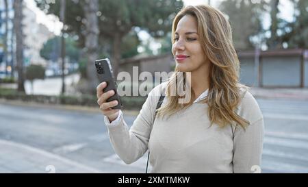 Young hispanic woman using smartphone on a sunny urban street Stock Photo