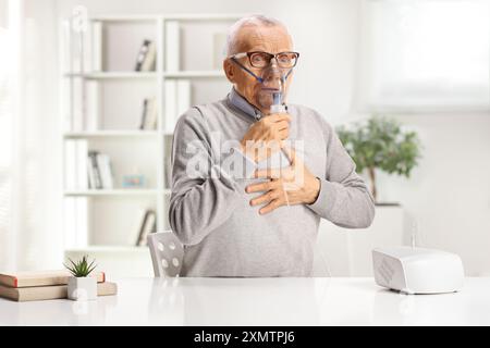 Elderly man sitting at a table and using a nebulizer at home Stock Photo