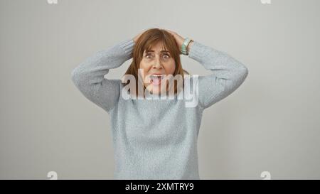 A surprised mature woman with short hair against an isolated white background expressing shock with hands on head. Stock Photo