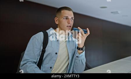 A young hispanic man holds a voice recorder in a university library, portraying a focused student indoors. Stock Photo