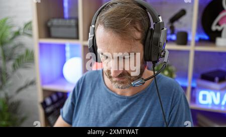 Middle-aged man with beard wearing headset in a gaming room at night. Stock Photo