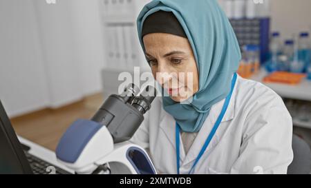 A mature woman in a hijab conducting research using a microscope in a laboratory setting Stock Photo