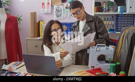Two women collaborating in a tailor shop among sewing machine, fabrics, and laptop Stock Photo