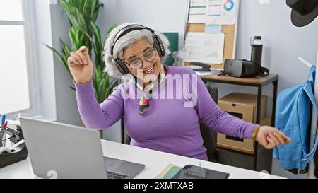 A joyful middle-aged woman dances in her office, showcasing a beautiful, engaging moment of workplace happiness Stock Photo