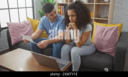 A concerned couple sits together in their living room, with a man and woman examining documents, reflecting relationship and family issues indoors. Stock Photo