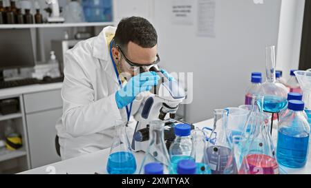 A hispanic man in a lab analyzing samples through a microscope, showcasing science, research and healthcare. Stock Photo