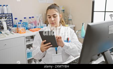 A focused hispanic woman uses a tablet in a laboratory setting, portraying modern healthcare technology. Stock Photo