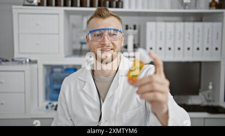 A smiling young caucasian man wearing glasses and a lab coat holding medication in a clinical setting. Stock Photo