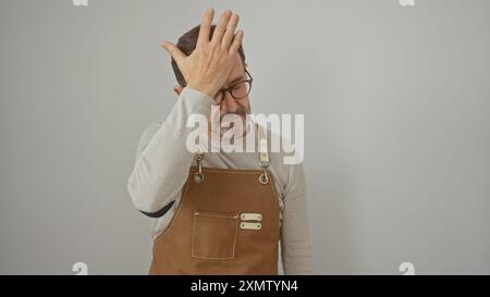 A mature man in an apron looking frustrated, touches his head against a white background. Stock Photo