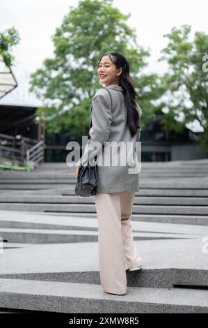 An attractive, positive Asian businesswoman is walking up the stairs in the city, looking away with a smile on her face, going to work. Stock Photo