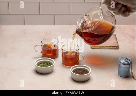Hand pouring tea from tea pot into glass cups, with brewing sieve and two kinds of tea Stock Photo