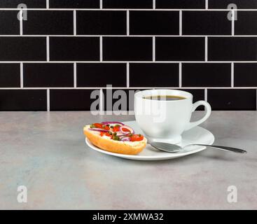 Coffee and bagel on white on pink tinged countertop with black subway tile background. Bagel is topped with cream cheese, tomato, red onion and capers Stock Photo