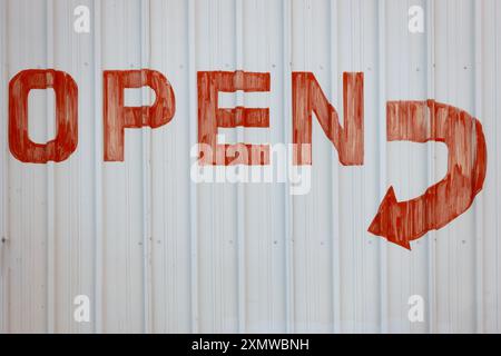 Old faded and weathered painted sign reading open in red on white metal with curving arrow pointing the way to the entrance Stock Photo