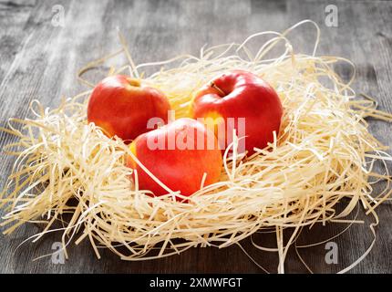 Three apples in straw on a table Stock Photo