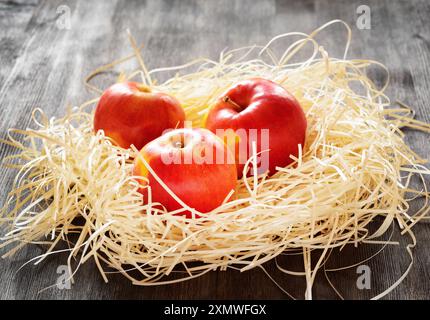 Three apples in straw on a table Stock Photo