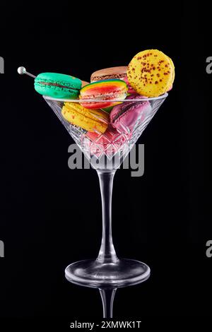 Vibrant, assorted macarons displayed elegantly in a martini glass against a black background, showcasing a creative dessert presentation. Stock Photo