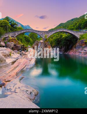 A vertical 4:5 image from a summer sunrise at the Ponte dei Salti bridge. The old stony bridge (also called "Ponte Romano") spans the Verzasca river i Stock Photo