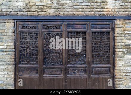 Ancient classic wooden door with typical Chinese architecture style pattern and woodcarving against brick wall Stock Photo