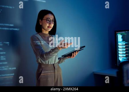 asian woman programmer standing in front of a screen with code projected  presentation the integration of technology and human expertise in software d Stock Photo