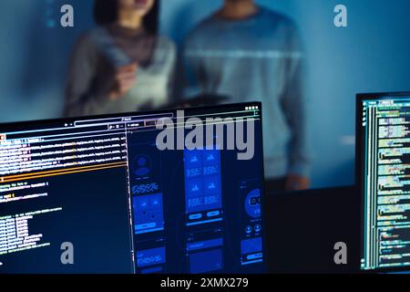 UX designer works on a tablet while a colleague tests  application in the background in office Stock Photo