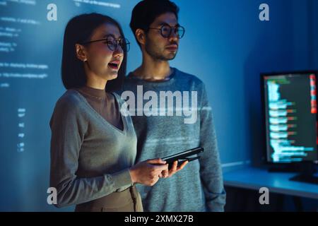 Asian Two software developers engaged in collaborative coding session, with code projected onto the wall and multiple computer screens displaying Stock Photo