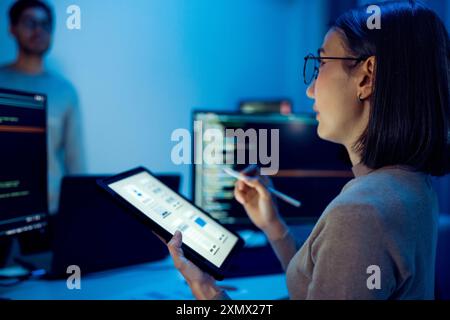 UX designer works on a tablet while a colleague tests  application in the background in office Stock Photo