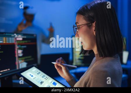 Asian UX designer works on a tablet while a colleague tests a VR application ,integration of user experience design and virtual reality development in Stock Photo
